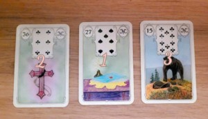 Trois cartes du White Owl Lenormand c&ocirc;te &agrave; c&ocirc;te sur du parquet: La Croix, la lettre et l&rsquo;ours
